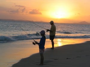 Man and boy fishing from a beach practicing patience